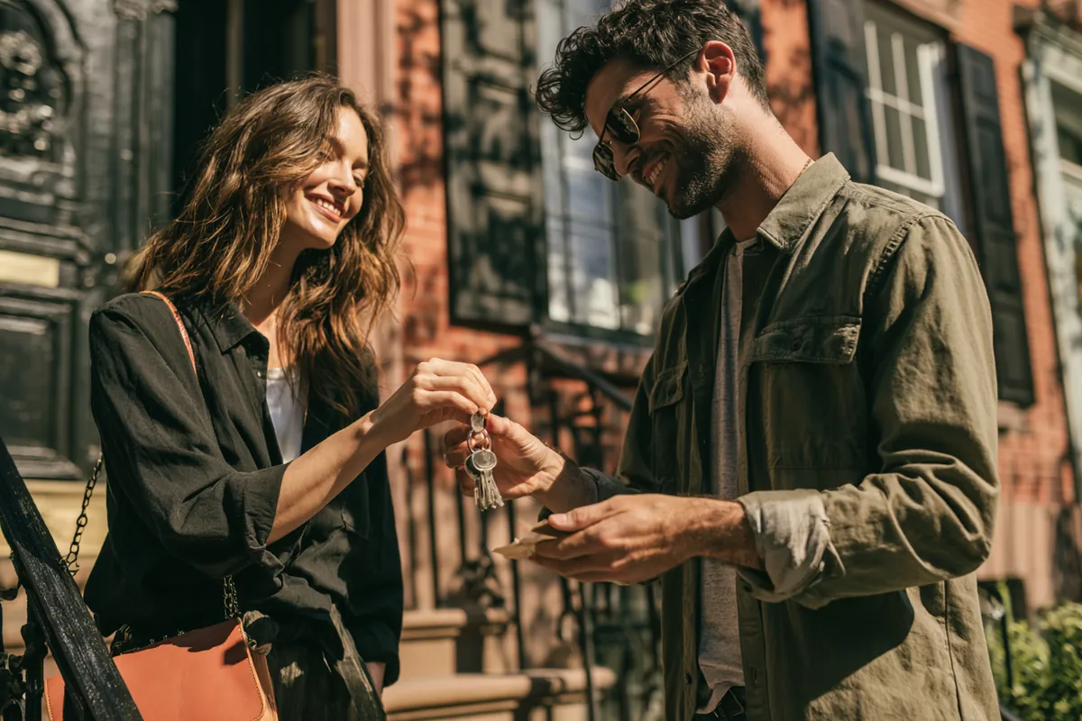 Man handing house keys to a smiling woman on the front step of a townhouse, a move-in Uplyft Capital helped fund